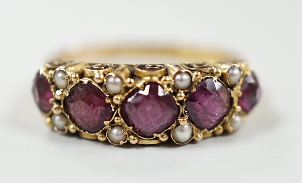 A late Victorian 15ct gold and graduated five stone garnet set half hoop ring, with split pearl spacers, size, P/Q, gross weight 2.5 grams.